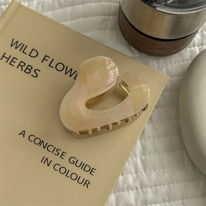 Detail view of heart-shaped cream marble claw clip with golden metal teeth on vintage books
