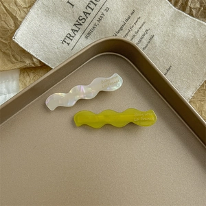 Detail of two wavy acetate hair clips in pearl white and lime green on a vintage tray