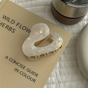 Detail of pearlescent acetate hair claw clip with gold metal teeth on book background
