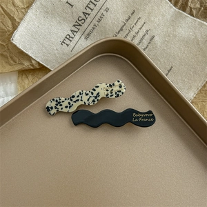 Close-up of wavy acetate hair clips in black and spotted beige on a metal tray