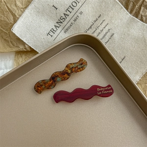 Detail of wavy acetate hair clips in amber and dark red on a golden vintage tray