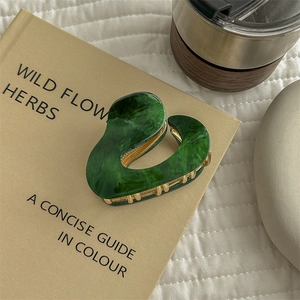 Detail of green marble acetate hair claw with gold metal teeth on a vintage book