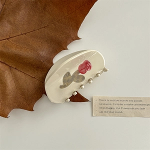 Detailed view of cream-colored claw clip with red rose pattern on a clean white background