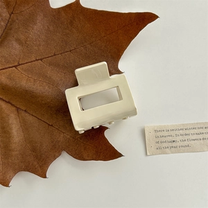 Close-up of a milky white square hollow hair claw clip resting on brown autumn maple leaves