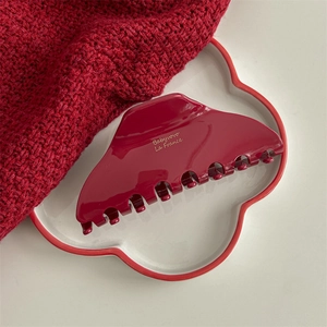Close-up of a deep burgundy acetate hair claw clip with gold lettering on a red knit textile