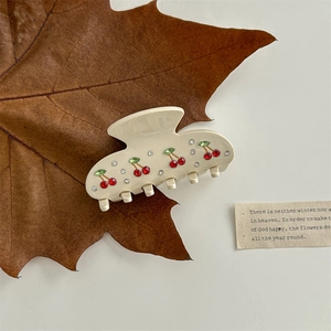 Detail of cream hair claw clip with cherry rhinestones on a natural autumn leaf background