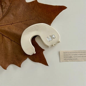 Detail of cream hair claw clip with H-letter and rhinestone on a decorative dry leaf