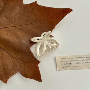 Detail view of a cream-white butterfly hair claw clip with glossy finish on vintage paper