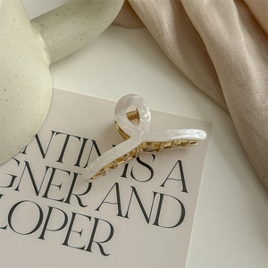 Detail of elegant white pearlescent acetate hair claw with a golden metal base