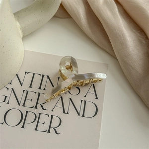 Detail of elegant cloud white hair claw clip with golden metal spring on silk fabric