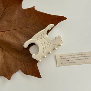 Detailed close-up of ivory acetate claw clip with vintage cross design on autumn leaf background
