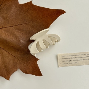 Detail view of a glossy cream hair claw clip placed on a dried leaf for an elegant look