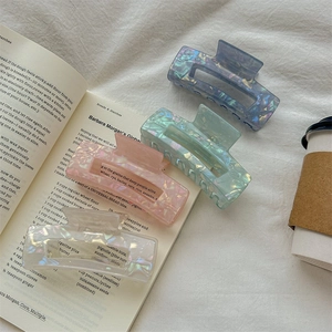 Iridescent mermaid-style hair claws in four colors on an aesthetic book background
