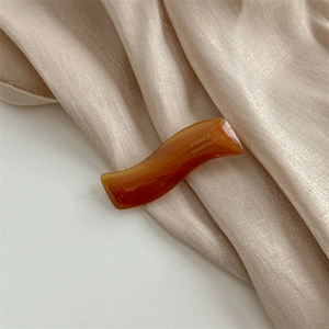 Détail d'une pince à cheveux ondulée en acétate ambré sur soie avec marquage France Handmade