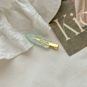 Detail of a light cyan marble textured hair clip with gold metal base on background