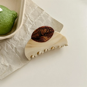 Close-up of a 7.5cm acetate hair claw with cream marble and wood grain texture patterns