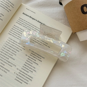 Close-up of iridescent pearl white hair claw clip placed on a book with soft lighting