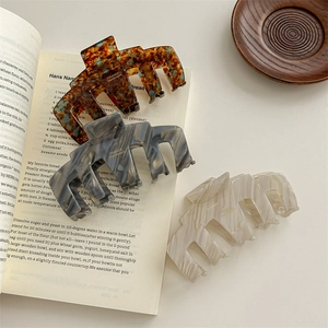 Three acetate hair claws with marble patterns displayed on an open vintage book