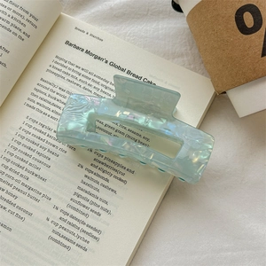 Detail of mint green pearlescent hair claw clip with marble texture on an open book
