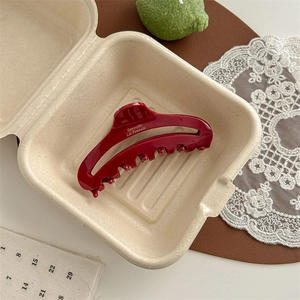 Detail of dark red acetate shark hair clip with gold label in a lifestyle gift box setting