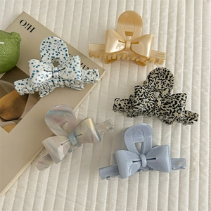 Set of five elegant acetate bow hair claws in diverse patterns on a white textured fabric