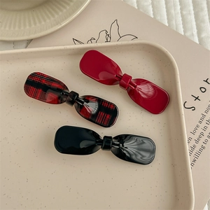 Trois barrettes nœuds en acétate rouge, à carreaux et noir sur un plateau décoratif