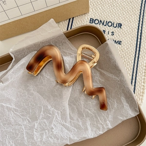 Détail macro de la pince à cheveux ondulée en acétate avec cadre en métal doré et fini ambre mat