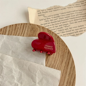 Détail de la pince à cheveux cœur rouge avec logo doré France Handmade sur un plateau vintage