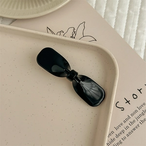 Détail d'une pince à cheveux noire brillante en acétate avec un design de nœud minimaliste