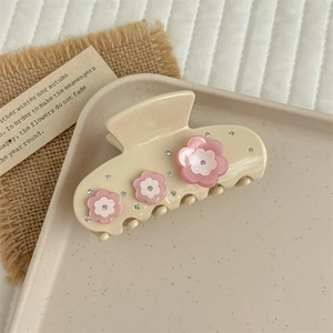 Detailed close-up of cream acetate hair claw with pink rhinestone flowers on fabric