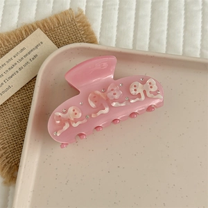 Close-up of pink acetate hair claw clip with pearly bow relief and small rhinestones
