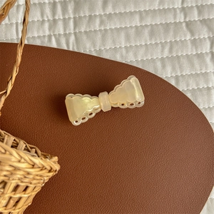 Detail showing the cream-colored acetate bow hair clip with decorative scalloped edges