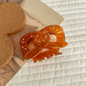 Macro detail of amber pretzel hair claw clip with white dots on soft fabric