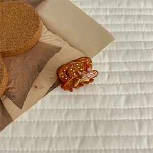 Detail view of large amber acetate hair claw clip with white dots on quilted background
