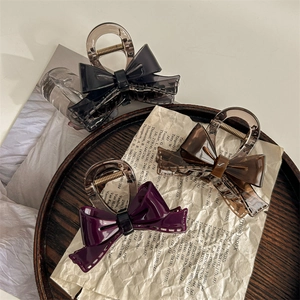 Three-piece French acetate bow hair claws in grey, amber, and purple on a vintage wooden tray