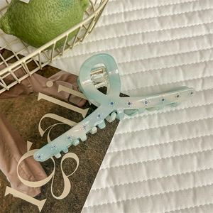 Détail d'une pince à cheveux verte en acétate avec strass bleus sur tissu blanc