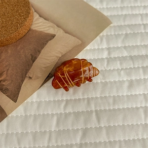 Detail shot of a large croissant hair claw clip with golden texture on soft fabric background