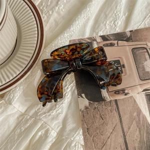 Detail showing acetate bow hair claw clip with vintage tortoiseshell texture and handmade logo