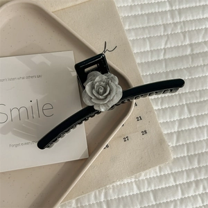 Detailed close-up of a large black hair claw clip with a marble texture camellia flower detail