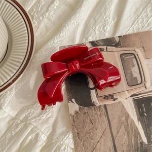 Detailed close-up of a red acetate bow hair claw clip with handmade lettering detail