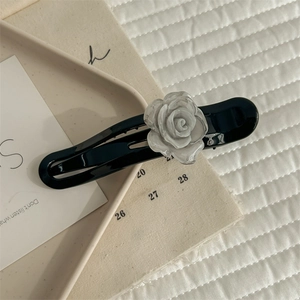 Detailed close-up of a glossy black acrylic hair claw clip with a white camellia flower