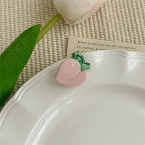 Détail d'une pince à cheveux en forme de pêche rose en acétate sur une assiette blanche