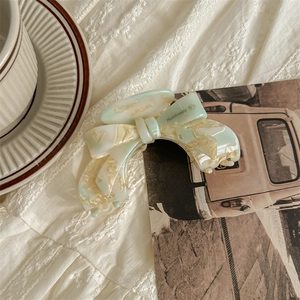 Detail of handmade acetate hair claw with green marble texture on white fabric