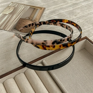 Three stylish resin headbands in black, tortoiseshell and pink on a beige fabric background