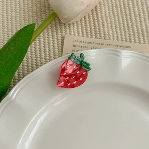 Détail d'une pince à cheveux fraise en résine d'acétate rouge sur une assiette blanche