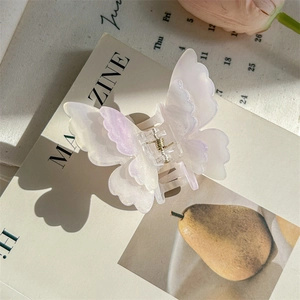 Gros plan d'une pince à cheveux papillon aux reflets irisés et finition perle sur magazine