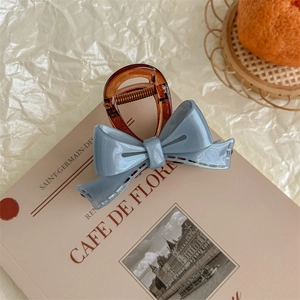 Close-up of a French grey acrylic bow hair claw clip on a minimalist book background