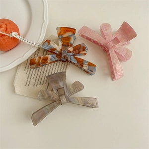 Three acetate bow hair claws in tortoiseshell pink and grey textures on a white tray