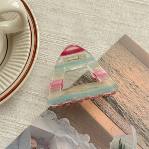 Detail of a minimalist triangular acetate hair claw with pastel stripes and hollow design