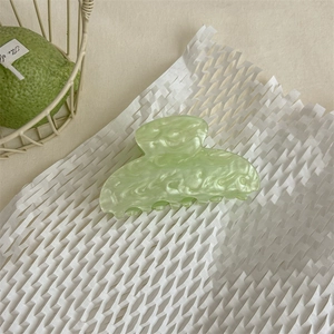 Vista dettagliata di una pinza per capelli in acetato marmorizzato verde chiaro su carta bianca